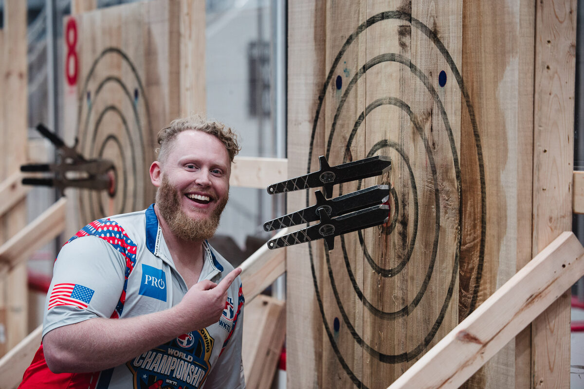 A WKTL competitor grinning beside three knives stuck in a target